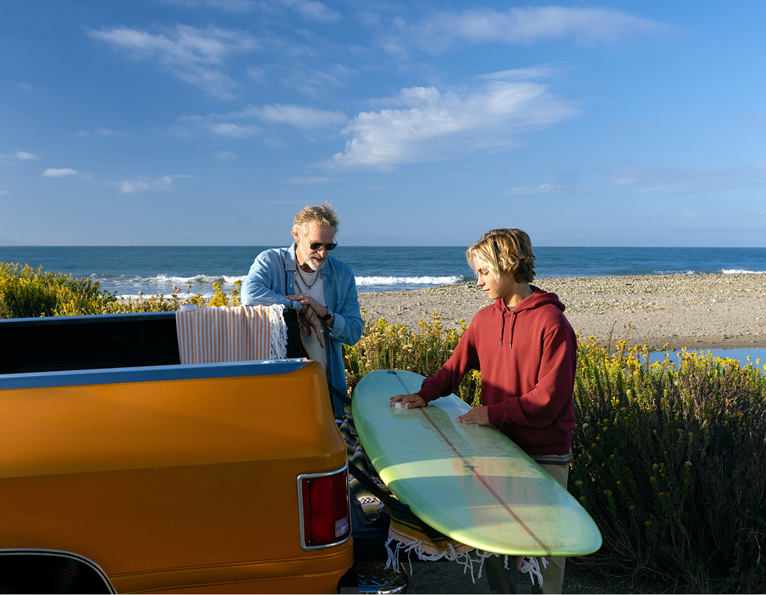 Grandfather and grandson waxing surfboard on orange truck