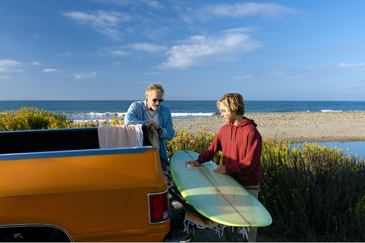Grandfather and grandson waxing surfboard on orange truck