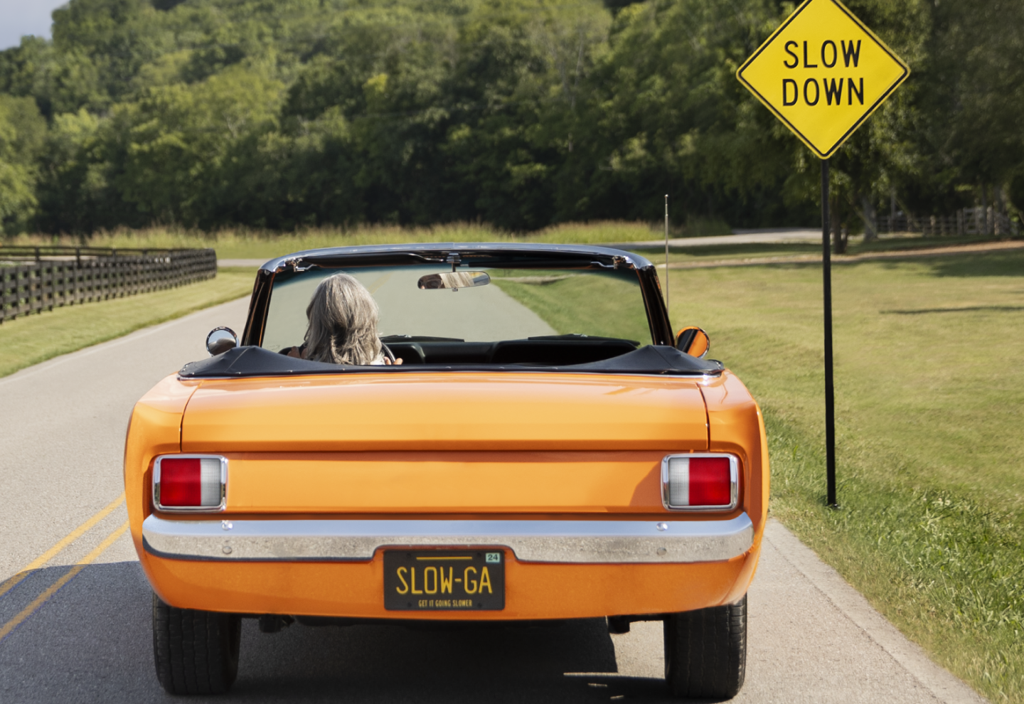 An orange car in front of a 'Slow Down' sign