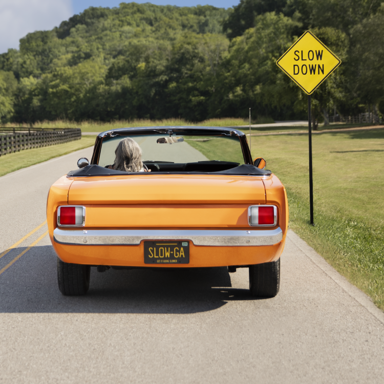 An orange car in front of a 'Slow Down' sign